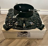 Image of vintage cast iron Christmas tree stand on top of its box showing decorative bells and garland design.