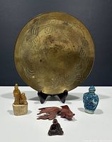 Front view of all items displaying brass dragon plate on stand, blue and white snuff bottle, carved figurines arranged in front.