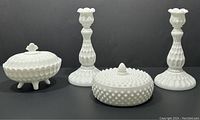 Full view of the four Fenton milk glass pieces: footed oval candy dish with lid, flat round candy dish with lid, and pair of candlesticks.