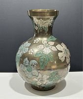 Front view of vintage brass vase with raised floral decoration in silver and green.