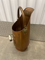 Side view of the tall copper pitcher showing brass handle with decorative lion head detail and white wrapped side handle for grip.
