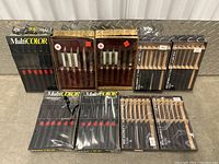 Photo showing nine sealed cutting tool packages including MultiCOLOR black handle knives and multiple blade sets in wooden and plastic packaging.