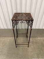 Full front view of decorative metal side table showing ornate scrollwork on tabletop and apron with slender legs.