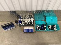 Full view of the lot showing essential oil bottles, blue glass bottles, and boxed pipette droppers on industrial floor with metal diamond plate background.