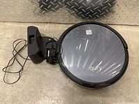 Eufy robot vacuum next to its black charging dock and power adapter on a floor surface with diamond plate metal background.