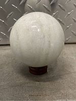 Front view of the large white crystal stone sphere on its wooden stand, showing smooth texture and subtle veining.