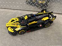 Side view of the yellow and black Lego Technic race car model showing detailed front and side components including wheels and decals.