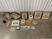 Full lot overview showing framed prints, ceramic pieces, wooden items, and small art cards arranged on floor