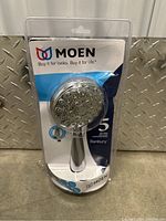 Moen Banbury shower head in original sealed blister packaging, showing front view and branding.