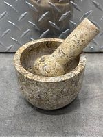 Marble mortar and pestle set showing mortar with pestle resting inside, beige marble with natural veining.