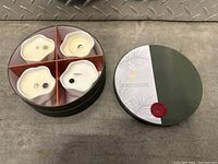 Round green box containing four white candles each with gemstone embedded in wax.