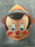 Front view of Pinocchio paper mask with colorful printed face and 'PINOCCHIO' on the hat