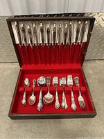 Full view of the wooden box open with all silverware neatly arranged inside red velvet lining.