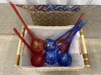 Photo showing six vintage glass ornaments inside a lined basket, three in red shades and three in blue shades.