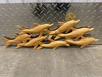 Wooden dolphin wall art carved in a group swimming pose, set against a metal diamond plate background.