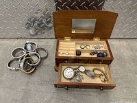Photo showing watch and jewelry lot displayed on floor, wooden box open revealing jewelry and watches, watch bands visible separately