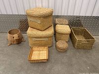 Lot of eight assorted wicker and woven baskets and containers arranged on tabletop against wall.