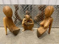 Set of three faceless wooden abstract human form sculptures on metal background showing frontal view