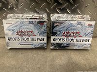 Two sealed Yu Gi Oh Ghosts From The Past booster boxes side by side on a metal surface, both unopened and shrink-wrapped