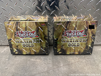 Two sealed Yu Gi Oh Maximum Gold boxes side by side against diamond plate metal background.
