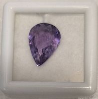 Close-up of a pear-shaped purple amethyst gemstone in a white display case.
