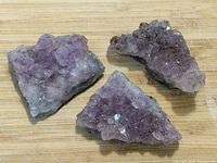 Clear image showing three amethyst crystal cluster pieces with natural purple crystal formations and base rock matrix on a wooden surface.