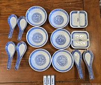 Top down image showing all items including 8 small round dishes, 6 porcelain spoons, and 3 rectangular chopstick rests arranged on a wooden surface.
