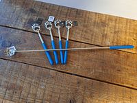 Five new extendable back scratchers with blue handles and bear claw heads laid out on wooden surface.