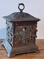 Front and side views of the cast iron lantern showing detailed floral and leaf decorative cut-outs and a ring on top for carrying or hanging.