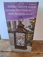 Photo of the lantern's box showing it is a holiday lantern with LED light in multiple languages, featuring a rustic lantern design.