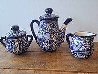 Full view of the three-piece blue and white glazed ceramic coffee set on wooden surface.