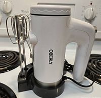 Side view of Oberly electric hand mixer on black circular stand with one type of stainless steel mixer attachment inserted.
