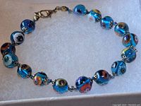 Image of the bracelet laid on soft white padding showing the blue glass beads with floral designs and metal clasp.
