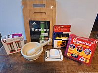 Photo of kitchen wares including salt and pepper set, bamboo cutting boards, ceramic mortar and pestle, egg slicer, Eggettes egg cooker, and spice holders staged on wooden surface.