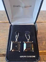 Pair of sterling silver earrings with large square citrine gemstones, displayed in black velvet box with 'Sterling Silver' and 'Genuine Gemstone' text.