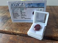 Oval cut red natural ruby gemstone in white display box with KGCL certificate card in background