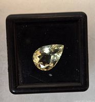 Clear image of a pear-shaped, pale yellow lemon quartz stone in a black display case.