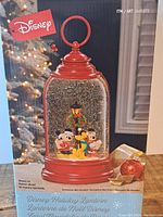 Photo of the box showing the Disney holiday lantern featuring Mickey Mouse, Pluto, and Donald Duck figurines inside with snow and light effects.