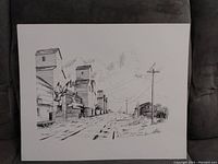 Single black and white print on white paper showing a rural landscape with large grain elevators, railroad tracks, and telephone poles. Artist signature visible on bottom left corner.