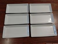 Top view of six white ceramic rectangular serving platters arranged in two columns of three on a wooden surface.