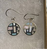 Close-up of the pair of sterling .925 silver earrings with colorful geometric inlay in pastel colors and small silver dots on circular drop, hooks visible.