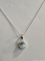 Close-up image showing the oval sky blue topaz pendant surrounded by cubic zirconia stones on a rhodium plated sterling silver chain.