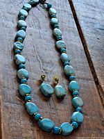 Turquoise stone necklace and matching earrings laid flat on a rustic wood surface showing the shape and color of the beads.