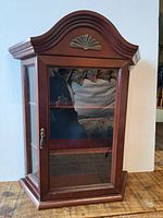 Front view of vintage wooden curio cabinet with glass panels and decorative top.