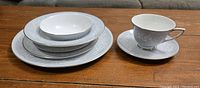 Set of stacked plates (dinner, salad, and bowl) alongside a teacup on saucer, all decorated with the gray band and white floral Valleyfield pattern by Royal Doulton.