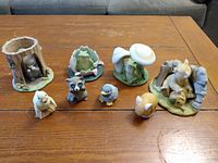Twelve porcelain figurines from the Woodland Surprises set displayed on a wooden table, showing variety of woodland animals and natural elements.