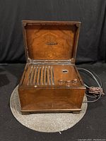 Front view of the open music box AM radio showing wooden varnished finish, horizontal slots, three wooden control knobs, and small dial indicator.