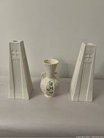 Full shot showing two white Art Deco inspired candle holders flanking Belleek Shamrock vase on white background.