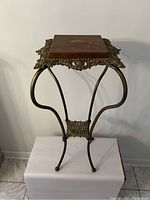 Front angled view showing entire brass frame with curved legs and wooden top part, highlighting filigree brass detailing surrounding the wooden surface.