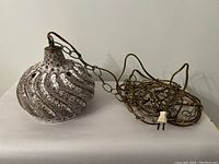 Full view of the swag lamp with ceramic shade and coiled metal chain and attached plug laid on surface